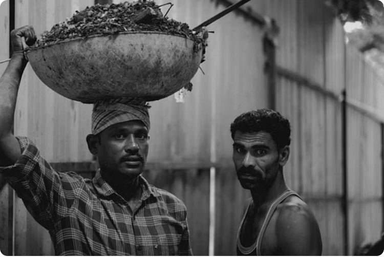 Black-and-white street photograph of two workers carrying loads, taken by a journalism and mass communication student at PES University