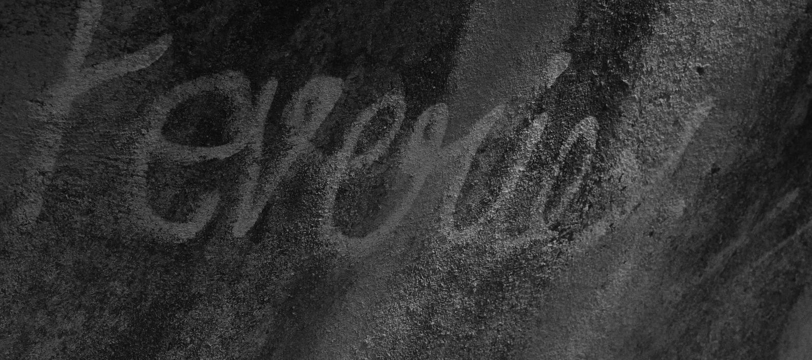 Black-and-white photograph of handwriting traced on a rough textured wall, taken by a journalism and mass communication student at PES University