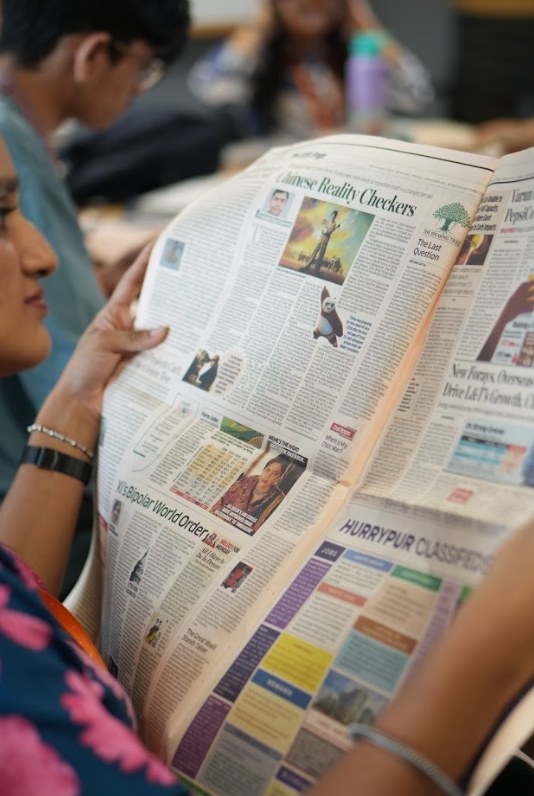 Student reading a broadsheet business newspaper during a print journalism class at PES University