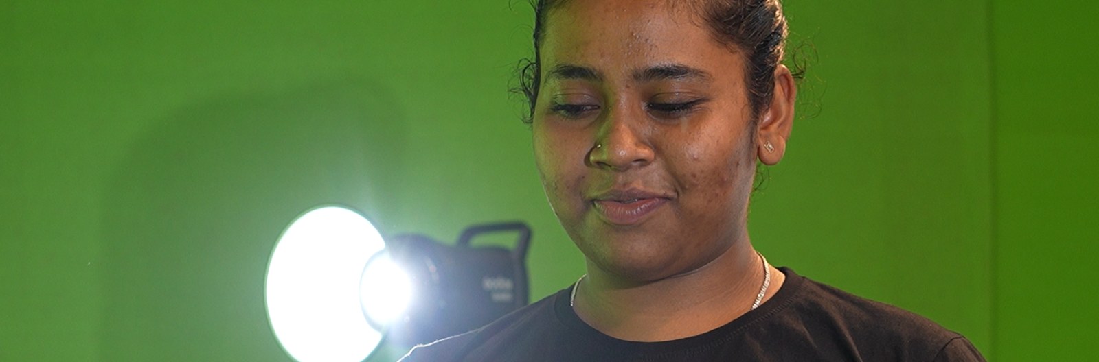 Journalism and mass communication student lit by a professional studio light against a green screen at PES University